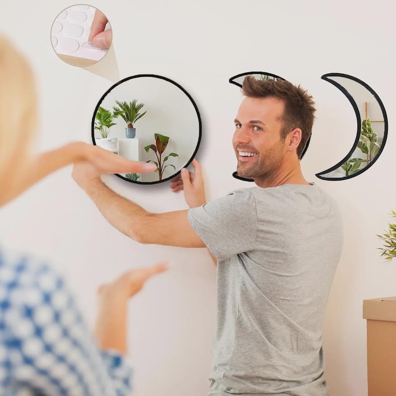 May include: A set of three wall mirrors with black frames, including one circular mirror and two crescent moon-shaped mirrors. The set includes small adhesive circular pads for mounting the mirrors to a flat surface for wall decoration.