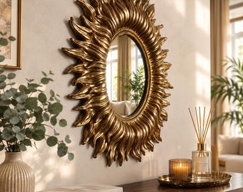 May include: An oval wall mirror with a metallic gold frame shaped like radiating sun rays. The frame features deep, textured grooves that create a sense of movement and depth around the central reflective glass surface.