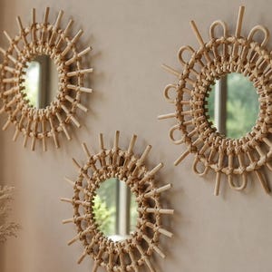 May include: Three circular wall mirrors featuring light brown woven rattan frames. Each mirror has a sunburst design with alternating straight spokes and looped rattan accents surrounding the central glass reflective surface.