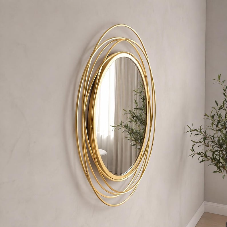 Peut inclure: Un miroir mural circulaire dot&eacute; d'un cadre dor&eacute; compos&eacute; de plusieurs anneaux m&eacute;talliques fins superpos&eacute;s. La surface en verre r&eacute;fl&eacute;chissant est centr&eacute;e dans le cadre, cr&eacute;ant un design concentrique en couches qui s'&eacute;tend vers l'ext&eacute;rieur.