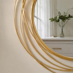 Peut inclure: Un miroir mural circulaire dot&eacute; d'un cadre en or poli compos&eacute; de multiples anneaux m&eacute;talliques incurv&eacute;s et superpos&eacute;s, cr&eacute;ant un effet orbital en couches. La surface en verre r&eacute;fl&eacute;chissant capture une commode blanche et une plante verte.