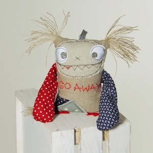 May include: A handmade plush toy with a stitched-on face and the words "GO AWAY" on its chest. The toy is wearing a red and white polka dot scarf and a blue and white patterned scarf.