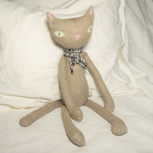 May include: A handmade plush cat toy with a gray linen body, pink nose, and green eyes. The cat is wearing a black and white checkered scarf.