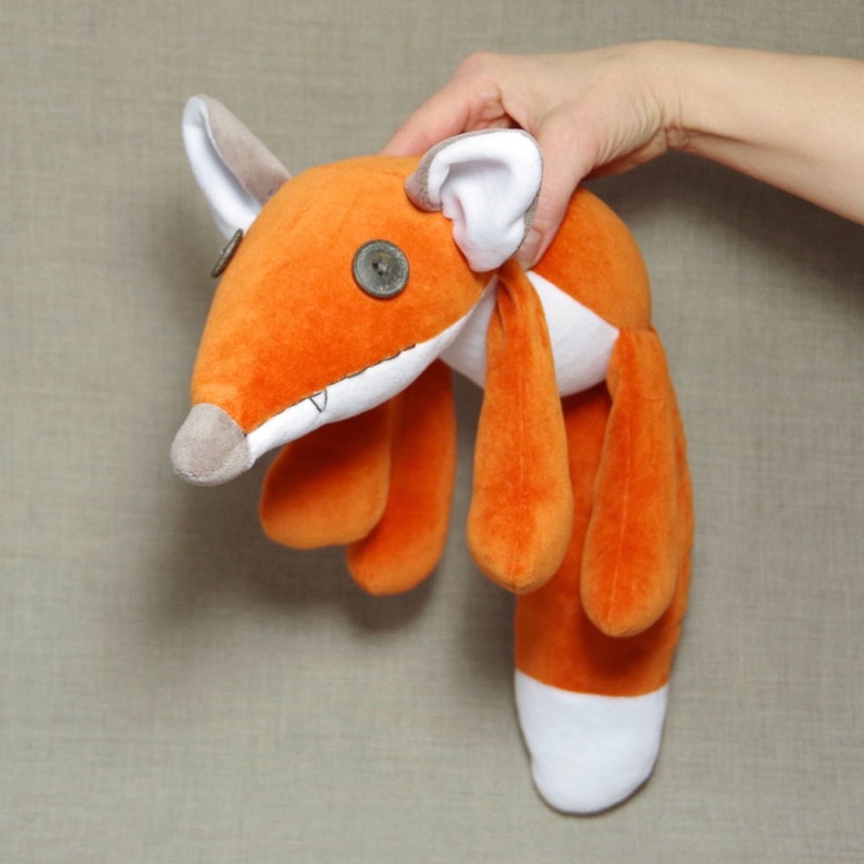 May include: Orange and white plush fox toy with button eyes. The fox has a long tail and four legs.