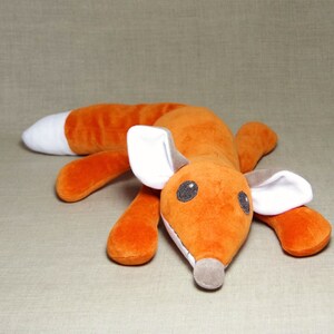May include: A plush orange fox toy with white ears and a white belly. The fox is lying on its belly with its head turned to the side.
