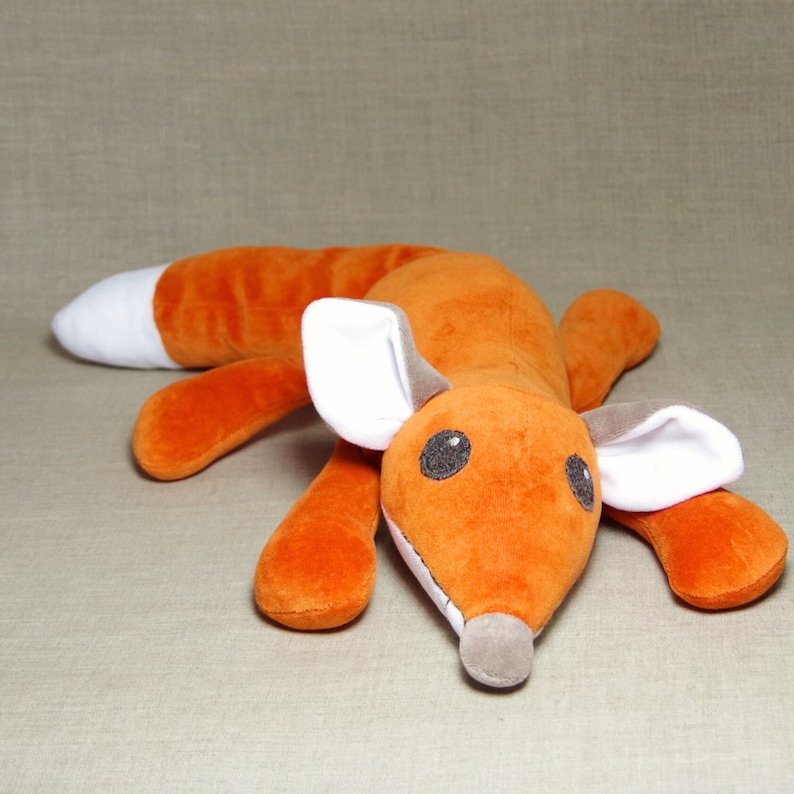 May include: A plush orange fox toy with white ears and a white belly. The fox is lying on its belly with its head turned to the side.