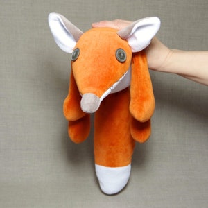 May include: A plush orange fox toy with white accents and button eyes. The fox is lying on its back with its legs in the air.