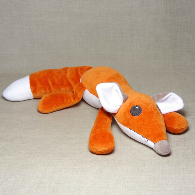 May include: A plush orange fox toy with white ears and a gray nose. The fox is lying on its belly with its head turned to the side.