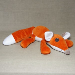 May include: A plush orange fox toy with white accents on the ears and tail. The fox is lying on its side with its head turned to the side.