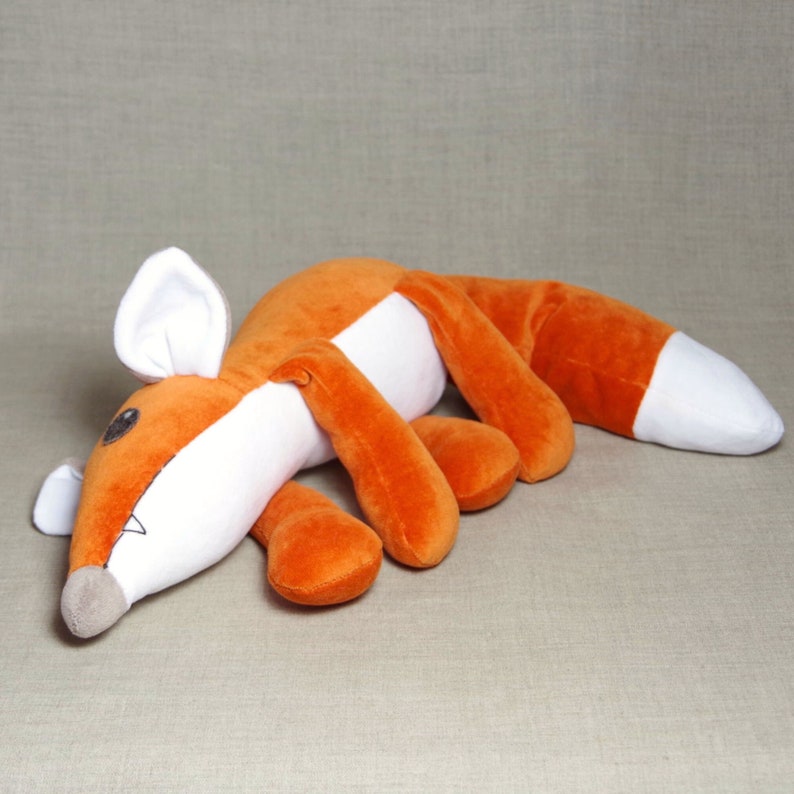 May include: A plush orange and white fox toy with a long tail and a white belly. The fox is lying on its side with its head resting on the ground.