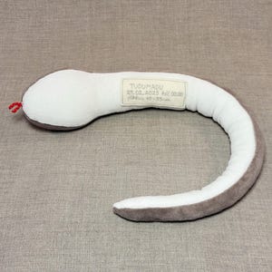 May include: A grey and white plush snake toy with a tag that reads "TUDUMADU 29.02.2025 full 00.00  Piikkus 45-55 cm".