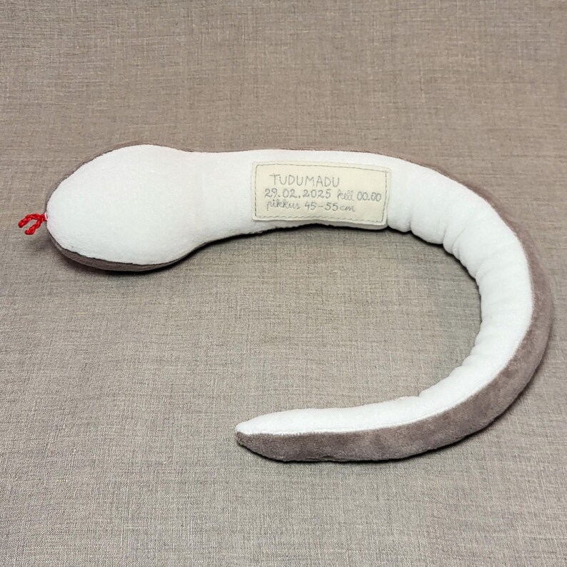 May include: A grey and white plush snake toy with a tag that reads "TUDUMADU 29.02.2025 full 00.00  Piikkus 45-55 cm".