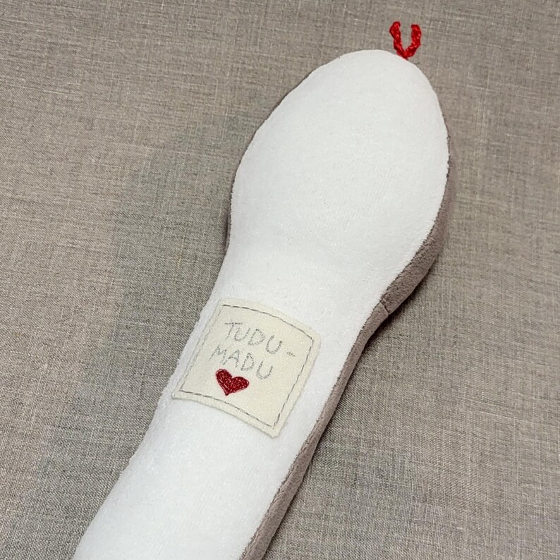 May include: A white plush toy shaped like a long, thin snake with a red heart embroidered on a tag that says "TUDDU - MADU".