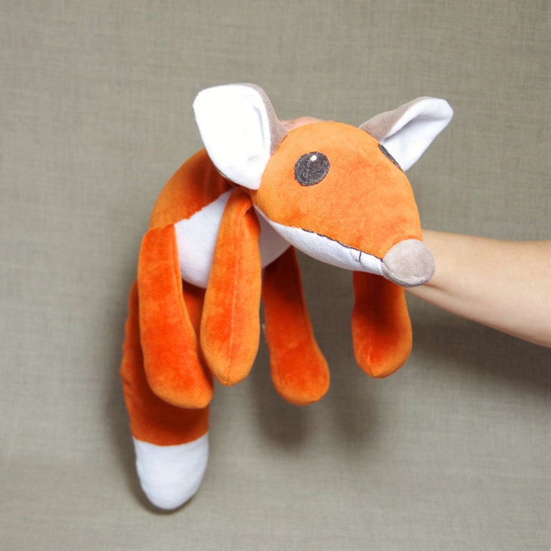 May include: Orange and white plush fox toy with a long tail. The fox has a brown nose and black eyes.