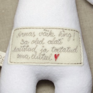 Puede incluir: Juguete de peluche blanco con una etiqueta cosida que dice "Armas v&auml;ike hing! Sa oled alati kaitstud ja toetatud oma eluteel." con un coraz&oacute;n rojo.