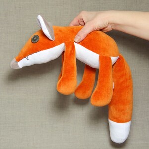May include: Orange and white plush fox toy with a button eye. The fox is lying on its side with its tail curled up.