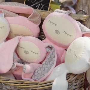 Puede incluir: Una cesta llena de juguetes de peluche rosa y blanco. Los juguetes tienen ojos bordados y tienen forma de conejos.