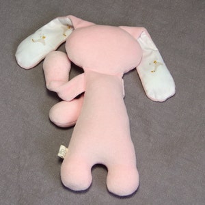 Puede incluir: Juguete de peluche rosa en forma de conejo con orejas de tela blanca. Las orejas tienen un peque&ntilde;o dise&ntilde;o bordado de un p&aacute;jaro.