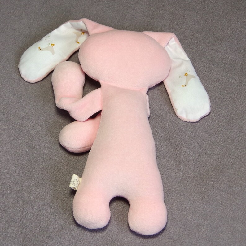 Puede incluir: Juguete de peluche rosa en forma de conejo con orejas de tela blanca. Las orejas tienen un peque&ntilde;o dise&ntilde;o bordado de un p&aacute;jaro.