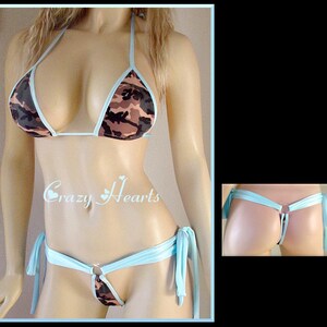 May include: A light blue bikini with a camouflage print top and a string bottom. The bikini has a ring detail at the center of the bottom.