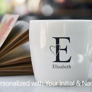 Pode incluir: Jarro de cerâmica branca com um "E" preto e um design de coração. O nome "Elizabeth" é impresso abaixo. O texto "Personalizado com sua inicial e nome" está na parte inferior.