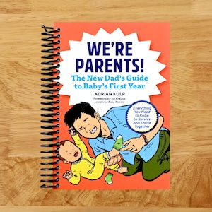 May include: A spiral-bound book titled "WE'RE PARENTS!" with the subtitle "The New Dad's Guide to Baby's First Year." The cover features an illustration of a father and baby. The book is orange with white and blue text.