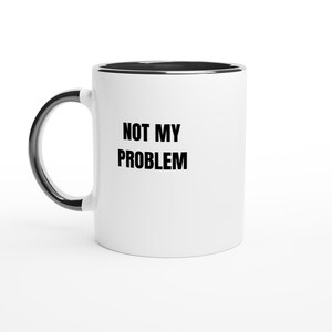 Może przedstawiać: Biały ceramiczny kubek z czarnym wnętrzem i czarnym uchwytem. Napis NOT MY PROBLEM jest wydrukowany pogrubionymi czarnymi wielkimi literami na przedniej stronie kubka. Kubek ma cylindryczny kształt z zakrzywionym uchwytem po lewej stronie.