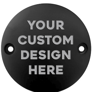May include: A black, circular metal plate with the text "YOUR CUSTOM DESIGN HERE" in raised, light gray lettering. The plate has two small holes and a matte finish.