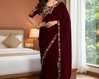 May include: A burgundy velvet saree with gold embroidery. The saree features a detailed floral pattern along the border and on the blouse. The sleeves are short, and the neckline is embellished with gold embroidery. The saree is draped elegantly.