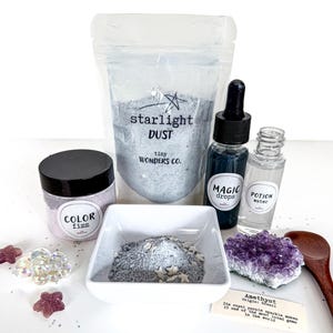 May include: A collection of mystical items including a bag of "Starlight Dust", a jar of "Color Fizz", and bottles labeled "Magic Drops" and "Potion Water". A small dish contains a mixture of powder and star-shaped sprinkles. An amethyst crystal and a wooden spoon are also present.