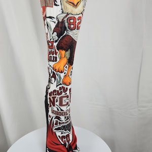 May include: A white knee-high athletic sock featuring a graphic print of an eagle mascot wearing a jersey with the number 82. The design includes red and maroon accents, text reading NCCU SCHOOL OF LAW, and additional sports-themed graphics.