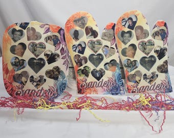 Puede incluir: Un conjunto de tres artículos de cocina: un guante de horno, un salvamanteles y otro guante de horno. Cada artículo está decorado con collages de fotos en forma de corazón y diseños florales. El nombre "Sanders" está escrito en cursiva en cada artículo.