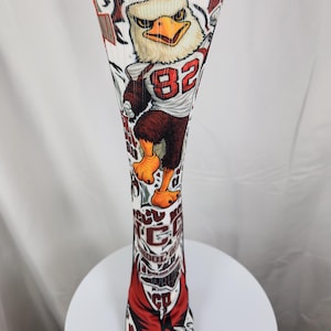 May include: A white knee-high athletic sock featuring a graphic of a cartoon eagle mascot wearing a jersey with the number 82. The sock includes red and black accents, with text elements reading NCCU, SCHOOL OF LAW, and DURHAM printed along the leg.