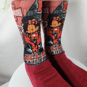 May include: A pair of red socks with a cartoon character design. The top of the socks features a graphic with a cartoon character, and the text "NCC EAGLES". The socks are made of a soft material.