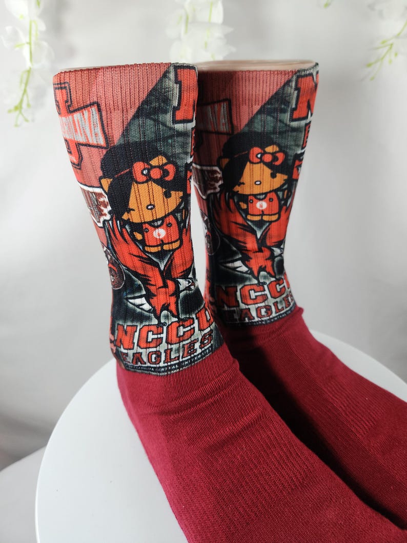 May include: A pair of red socks with a cartoon character design. The top of the socks features a graphic with a cartoon character, and the text "NCC EAGLES". The socks are made of a soft material.