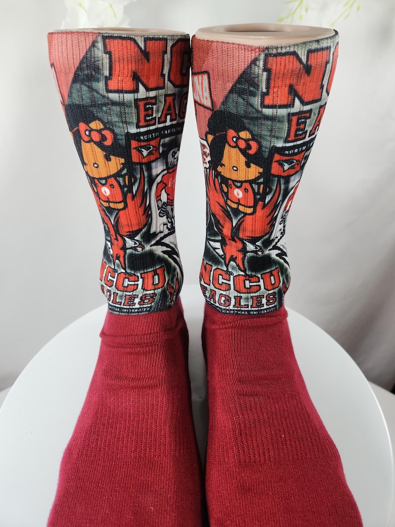 May include: Pair of red socks with a design featuring the letters "NCCU EAGLES" in orange and white. The socks have a cartoon eagle mascot and the words "NORTH CAROLINA" on them.