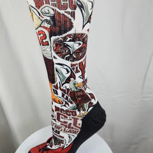 May include: A white crew sock featuring a repeating graphic print of the NCCU Eagles mascot, the number 12, and the text NCCU. The design includes red, black, and white colors, with a solid black heel and toe section, showcasing various eagle illustrations.