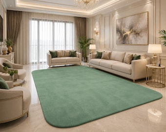 Puede incluir: Una alfombra grande y rectangular con esquinas redondeadas, que presenta un color verde salvia suave y sólido con una textura afelpada. La alfombra está colocada en el centro sobre un suelo pulido de color claro, sirviendo de punto focal.