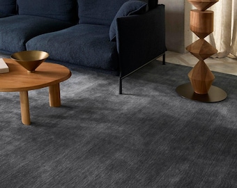May include: A large, rectangular area rug in a deep charcoal gray with a subtle, textured, linear grain pattern. The rug features a uniform, low-pile surface that covers the floor, providing a neutral foundation for the surrounding furniture.