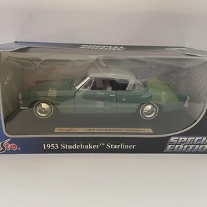 Könnte beinhalten: Ein grünes und graues Modellauto eines 1953 Studebaker Starliner in einer Displaybox. Das Modell ist eine Special Edition von Maisto, im Maßstab 1:18. Das Auto hat Chromräder und -verkleidungen und befindet sich in einer transparenten Kunststoffhülle.