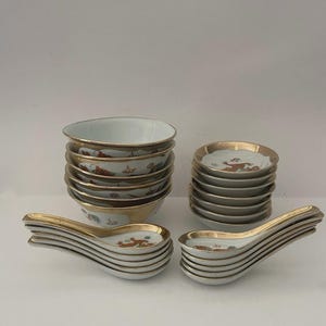 May include: A set of white porcelain tableware featuring a stack of six bowls, a stack of six small plates, and two stacks of six spoons. Each piece is decorated with orange and green patterns and finished with a metallic gold rim.