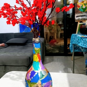 May include: A colorful, hand-painted vase filled with vibrant red floral branches. The vase is adorned with a patchwork design of blue, green, yellow, purple, and silver hues. The vase is a decorative item.