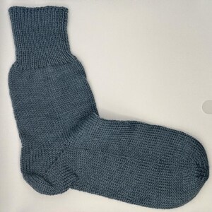 May include: A single, knitted sock in a muted blue-grey color. The sock features a ribbed cuff and a textured knit pattern throughout the body. The sock is designed for comfort and warmth.