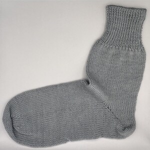 May include: A single gray knitted sock. The sock is made of a soft, textured yarn and features a ribbed cuff. The body of the sock has a smooth, even knit, and the heel and toe are well-defined.