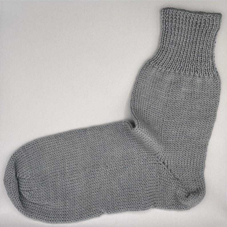 May include: A single gray knitted sock. The sock is made of a soft, textured yarn and features a ribbed cuff. The body of the sock has a smooth, even knit, and the heel and toe are well-defined.