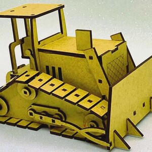 Op de afbeelding: Een geel houten bulldozer model met donkerbruine randen. De speelgoedbulldozer heeft een blad, rupsbanden en een cabine met een dak. Het model is gemaakt van uitgesneden houten stukken en in elkaar gezet om een 3D-effect te cre&euml;ren.