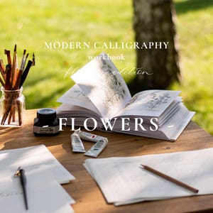 Op de afbeelding: Een houten tafel met kalligrafiebenodigdheden en een werkboek. Het werkboek is open op een pagina met botanische illustraties. De tekst luidt "MODERN CALLIGRAPHY workbook Flowers edition". Een pot met penselen, inkt en verftubes is ook aanwezig.