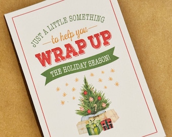 May include: A rectangular gift tag with a red border and the text "JUST A LITTLE SOMETHING to help you WRAP UP THE HOLIDAY SEASON!". The tag features a Christmas tree and wrapped gifts.