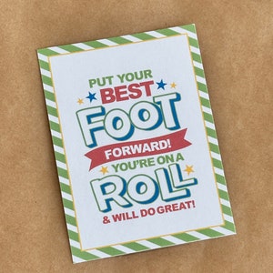 May include: A white card with green and yellow stripes on the border. The card has a motivational message that reads "Put your best foot forward! You're on a roll & will do great!" The text is in red, blue, and yellow.