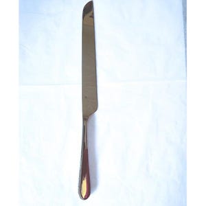May include: A polished silver-toned stainless steel dinner knife with a smooth, elongated handle and a slightly curved, pointed blade. The metal surface reflects light, showing a sleek, metallic finish throughout the entire utensil design.